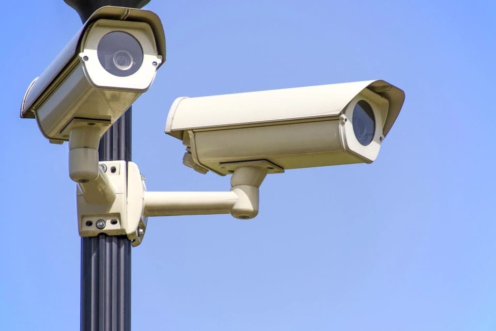 Two outdoor CCTV cameras mounted on a pole against a clear sky